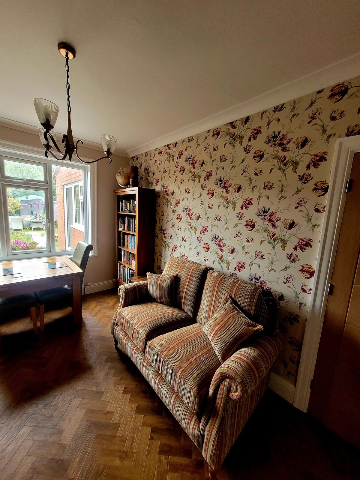 Dining room with a floral feature wallpaper wall, parquet floor and a striped sofa