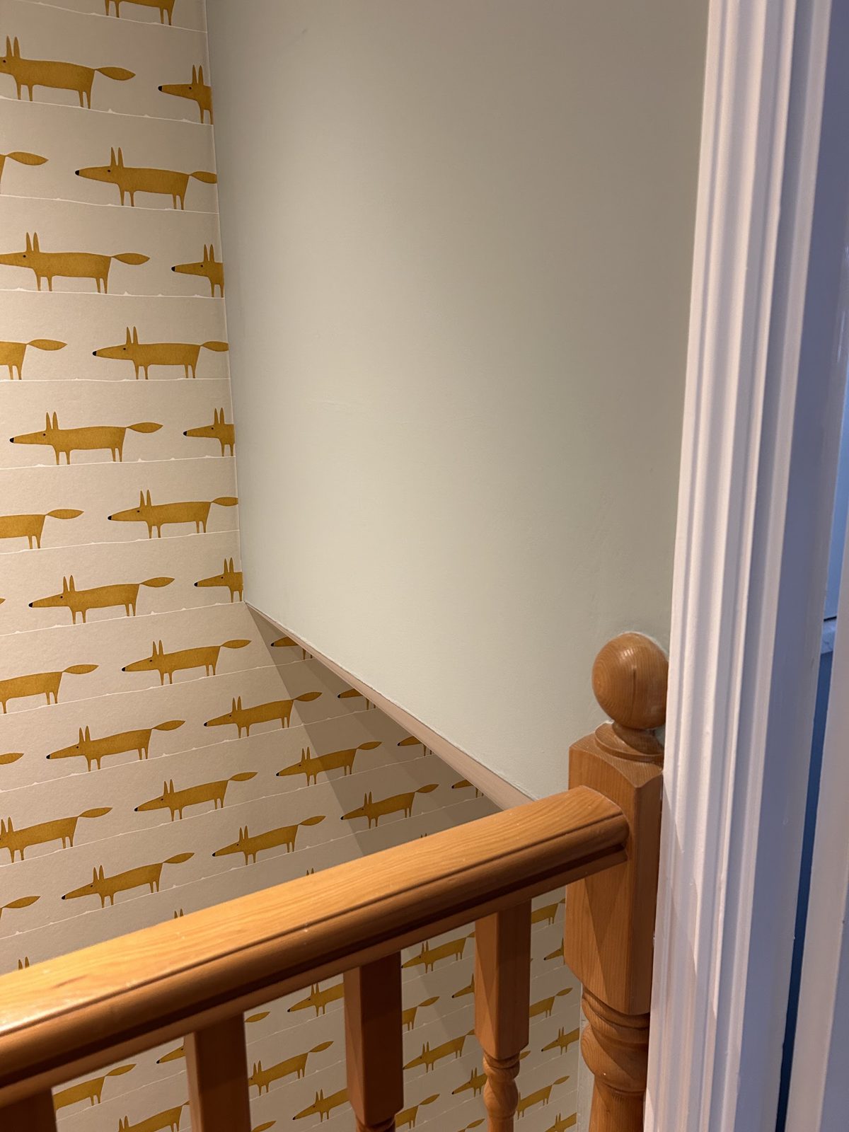 Hallway papered in a mustard fox-pattern wallpaper above an oak banister