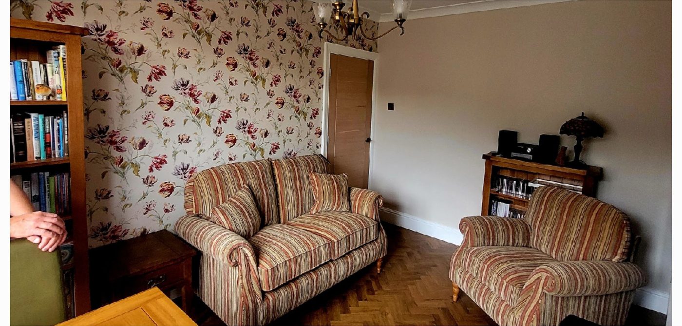 Living room after: floral feature wallpaper behind a striped sofa and armchair